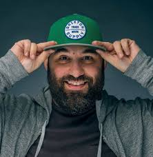 Bryan DeLuca smiling and tipping a green baseball cap